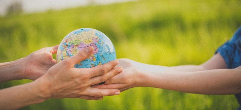 Na imagem vemos as mão de um adulto e as mãos de uma criança segurando um globo terrestre.